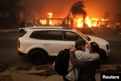 People hug as they leave the Eaton Fire in Altadena, California, on January 8, 2025, after high winds fueled the devastating wildfire in the Los Angeles area.